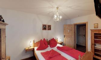A cozy bedroom with a double bed and red pillows. The walls are bright and there are wooden details and a ceiling lamp.