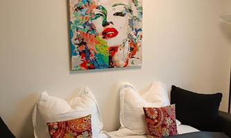 A stylish bedroom with a colorful artwork on the wall. Decorative pillows and a gray blanket are on the bed.