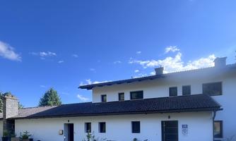 A modern building with white walls and a dark roof. The sky is blue and there are some clouds visible.