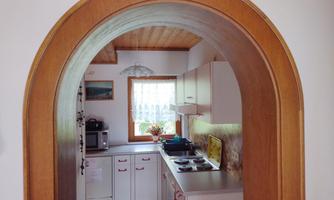 A cozy kitchen with a large window and modern appliances. The entrance is marked by a beautiful wooden arch.