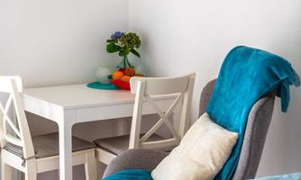 A bright room with a table and chairs as well as a cozy sitting area. Pictures hang on the wall and a plant stands on the table.