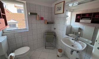A modern bathroom with tiles and a large mirror. There is a toilet, a sink, and shelves with towels.