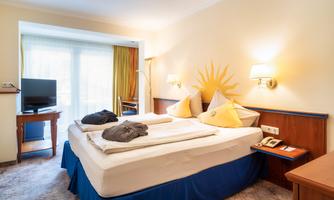 A cozy hotel room with two beds and soft colors. Large windows let in plenty of light and offer a view of the balcony.