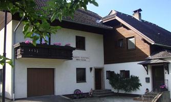 A beautiful house with two different facades, wooden cladding, and a balcony with flowers. The surroundings are clear and friendly.