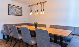 A modern dining room with a large wooden table and comfortable seating. Hanging lamps provide cozy light.