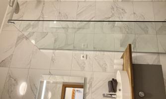 A modern bathroom with marbled walls and a glass shower. The washing area features a wooden countertop and a large mirror.