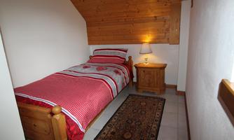 A cozy bedroom with a single bed and red-striped bedding. Next to the bed is a nightstand with a lamp.