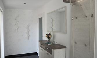A bright corridor with white walls and modern furniture. Visible are a mirror, a wall cabinet, and some wall hooks.
