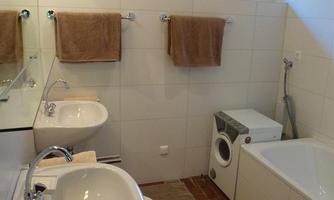 A modern bathroom with two sinks, a bidet, a bathtub. The walls are brightly tiled and the towels are neatly hung.