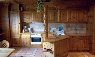 A cozy wooden kitchen with a central counter area. The walls are decorated with tiles, and there are modern kitchen appliances.