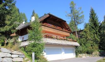 A cozy chalet with a balcony full of flowers. Surrounded by trees and clear skies.