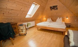 A cozy attic room with wooden paneling and a double bed. In daylight, the room radiates warmth and coziness.