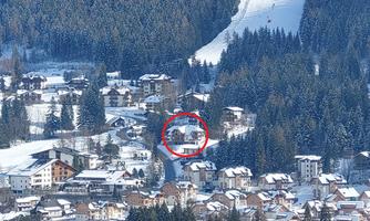 A snowy landscape with a small village and trees. In the foreground, a marked building can be seen, surrounded by winter nature.
