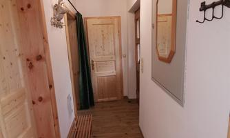 A bright hallway with wooden paneling and a bench. A mirror and coat hooks hang on the wall.