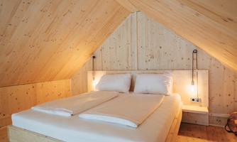 A cozy bedroom with wooden paneling and a double bed. The soft lighting creates a warm atmosphere.