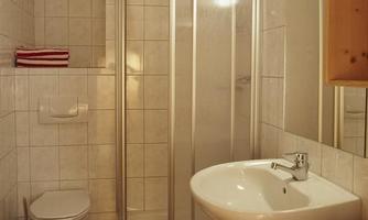 A simple bathroom with a shower, sink, and toilet. Red and white towels are decoratively hung.