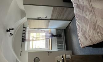 A cozy bedroom with a large bed, a TV, and a wardrobe. The window lets in plenty of daylight, and draped curtains create a homely atmosphere.