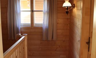 A bright hallway with wooden paneling and a railing. The windows are adorned with curtains, and a wall lamp provides cozy light.