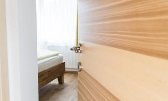 A half-open wooden door reveals a bright bedroom with a bed and a window. The room feels inviting and friendly.