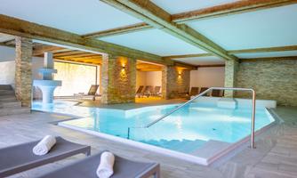 A modern spa with a heated pool and comfortable loungers. The walls are made of stone, and there is soft lighting for a relaxing atmosphere.