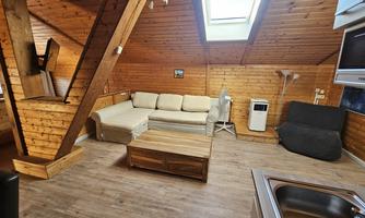 A cozy living space with wood paneling and a large window area. The room contains a sofa, a table, and a seating area.