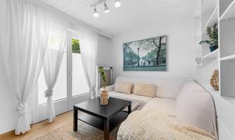 A bright living room with a cozy sofa and a table. Large windows with white curtains let in plenty of light.