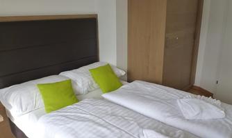 A cozy bedroom with a double bed and colorful cushions. The walls are light and the furniture is modern.