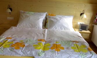 A cozy bedroom with a double bed and bright, colorful bedding. On the wall, there are two bedside lamps and a small television.