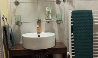 Bathroom with round washbasin on wooden cabinet, mirror, towels, toilet and tiled wall.