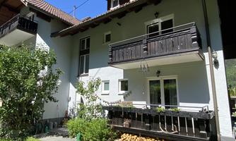A pretty house with a balcony and a beautiful garden. The facade is light and surrounded by trees.