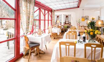 A bright restaurant with red windows and stylish tables can be seen. The decor is friendly and inviting, with flowers and decorative elements on the tables.
