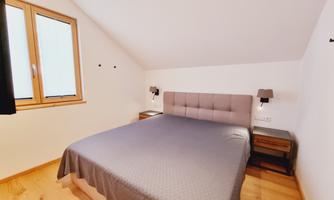 A cozy bedroom with a large bed and two nightstands. Large windows provide plenty of daylight.