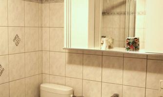 A small bathroom with white tiles. There is a sink, a toilet, and a mirror.