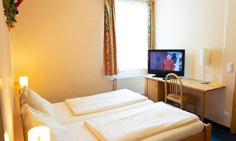 A cozy room with two single beds and a television. Bright colors and a window create an inviting atmosphere.