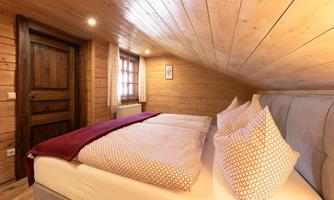 A cozy bedroom with wooden ceilings and warm tones. The bed is decorated with comfortable pillows and a blanket.
