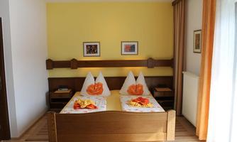 A cozy bedroom with a double bed and colorful pillows. The walls are painted in a warm yellow tone and there are decorative pictures.