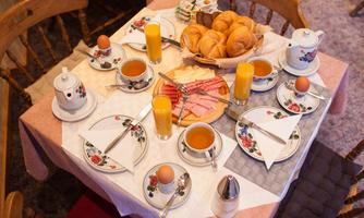 An inviting breakfast table with tea, eggs, bread, and cold cuts. The atmosphere is cozy and warm.