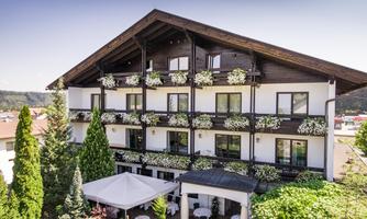 A stylish hotel building with balconies decorated with flowers. The garden is well-kept, and a pavilion invites relaxation.