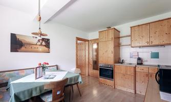 A cozy kitchen with wooden shelves and a dining table. The walls are bright, and a picture is decoratively hung.