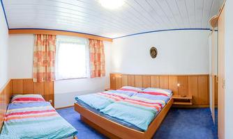 A cozy bedroom with three beds and colorful bedspreads. It has bright walls and a blue carpet.
