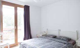 A bright bedroom with a large bed and checked bedding. Large windows let in plenty of light and provide a view outside.
