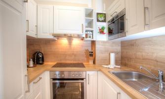 A modern kitchen with white cabinets and wood paneling. It is well-equipped with a stove, an oven, and a sink.