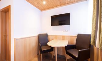 A small, cozy room with a table and two chairs. There is a television on the wall, and the walls are in light colors.