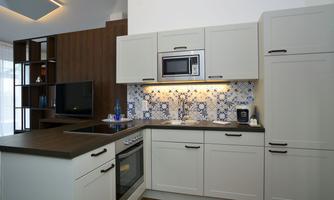 A modern kitchen with bright cabinets and an elegant tile design. The amenities include a stove, a microwave, and a TV corner.