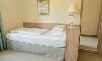 A simple bedroom with a single bed and a nightstand. The room has a bright and friendly atmosphere.