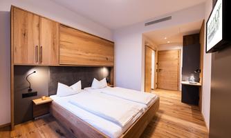 A modern bedroom with a double bed and wooden details. The walls are bright, and there is a cozy atmosphere.