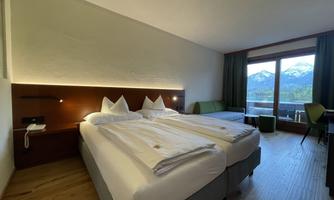 A modern hotel room with two beds and a large window. Outside, the mountains can be seen, creating a relaxed atmosphere.