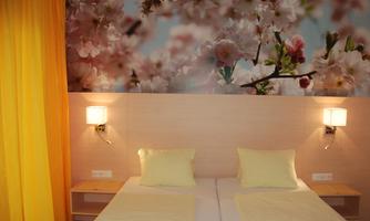 A cozy bedroom with two beds and soft yellow pillows. In the background, there is a beautiful floral pattern.