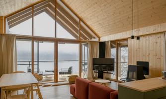 A modern, bright living room with a wooden ceiling and large windows. The view of the lake and the surrounding area is stunning.