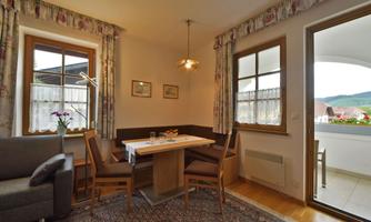 A cozy living area with a table and chairs. Large windows provide a view of the outside area.